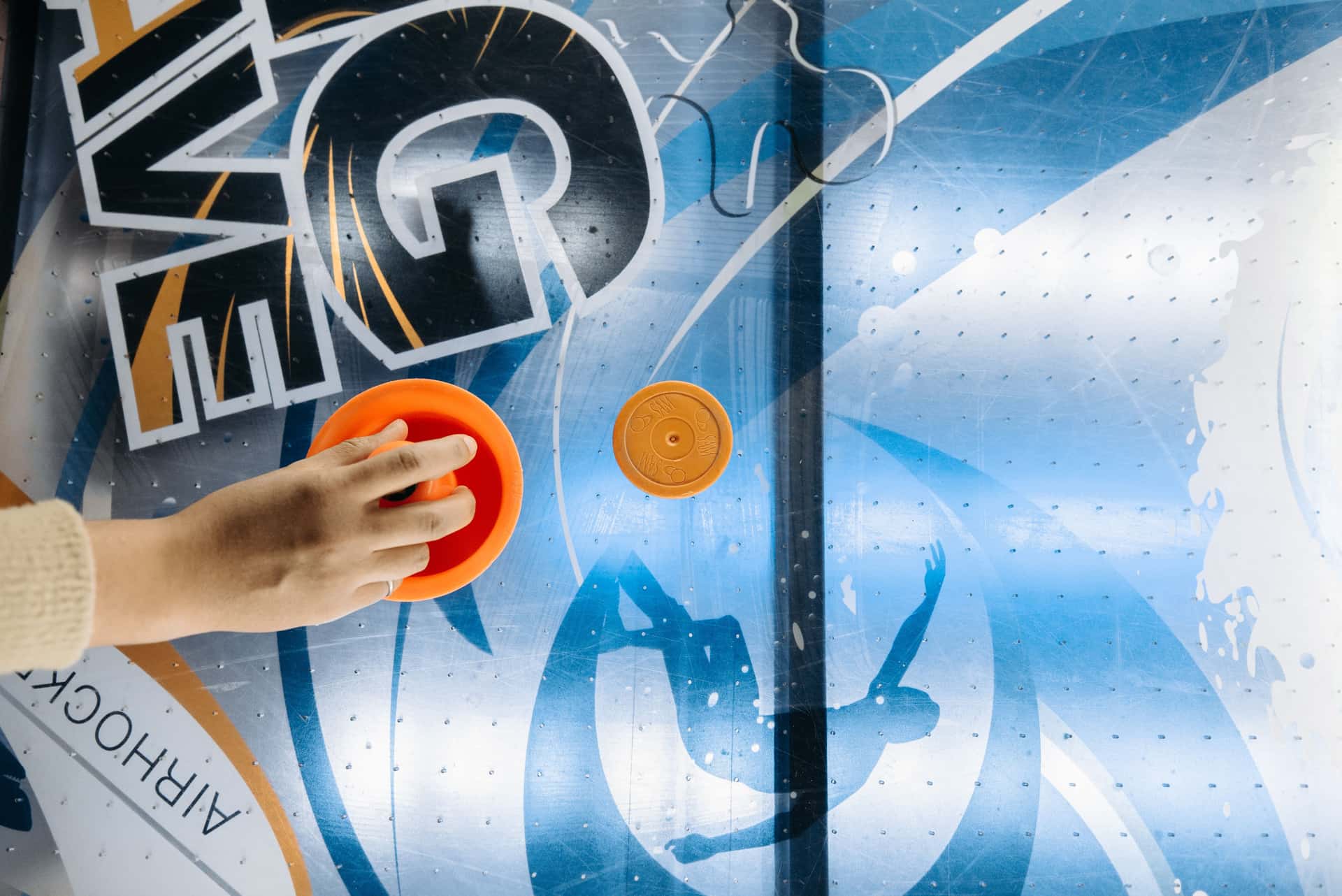 A hand playing air hockey, viewed from above