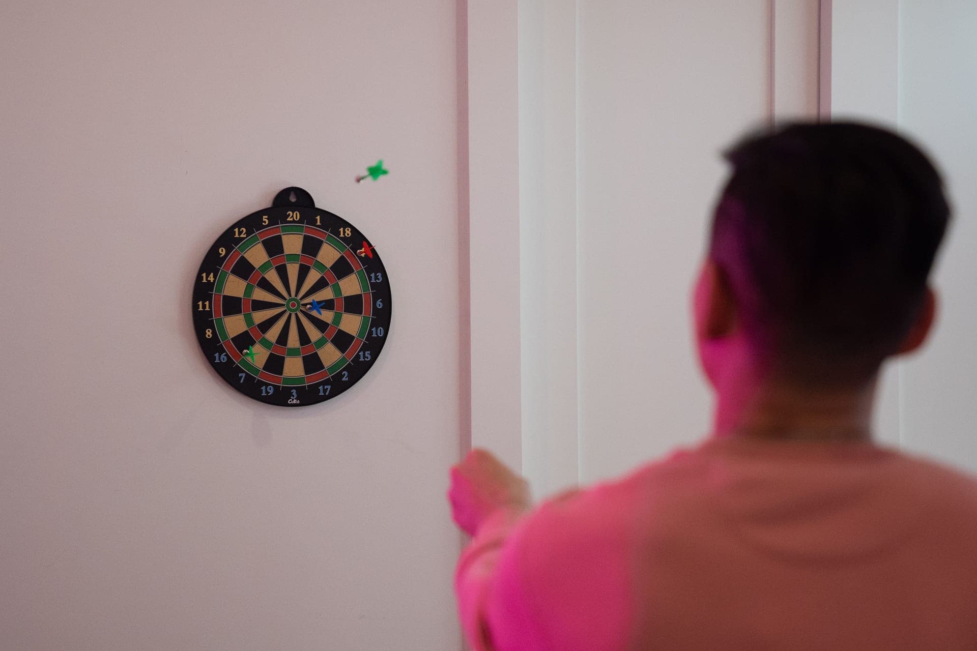 A person aiming a dart at a dartboard on a wall